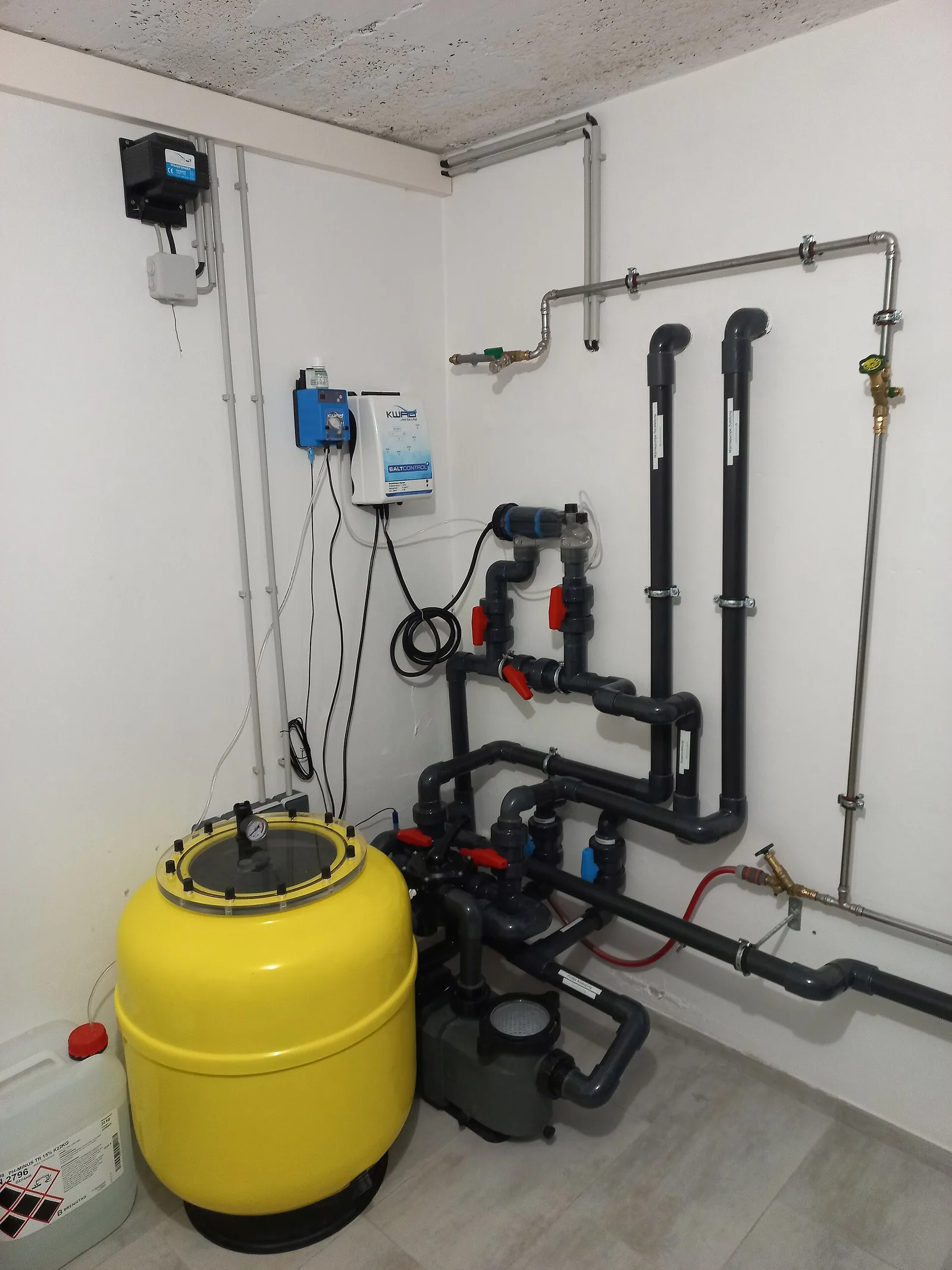 Swimming pool filter tank, pump, valves, and connected plumbing in an equipment room
