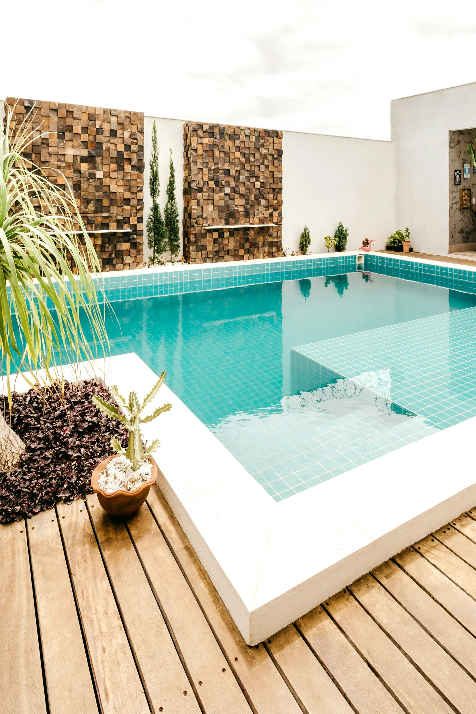 Landscaped pool edge with coping, wood decking, and planting beds arranged around the water