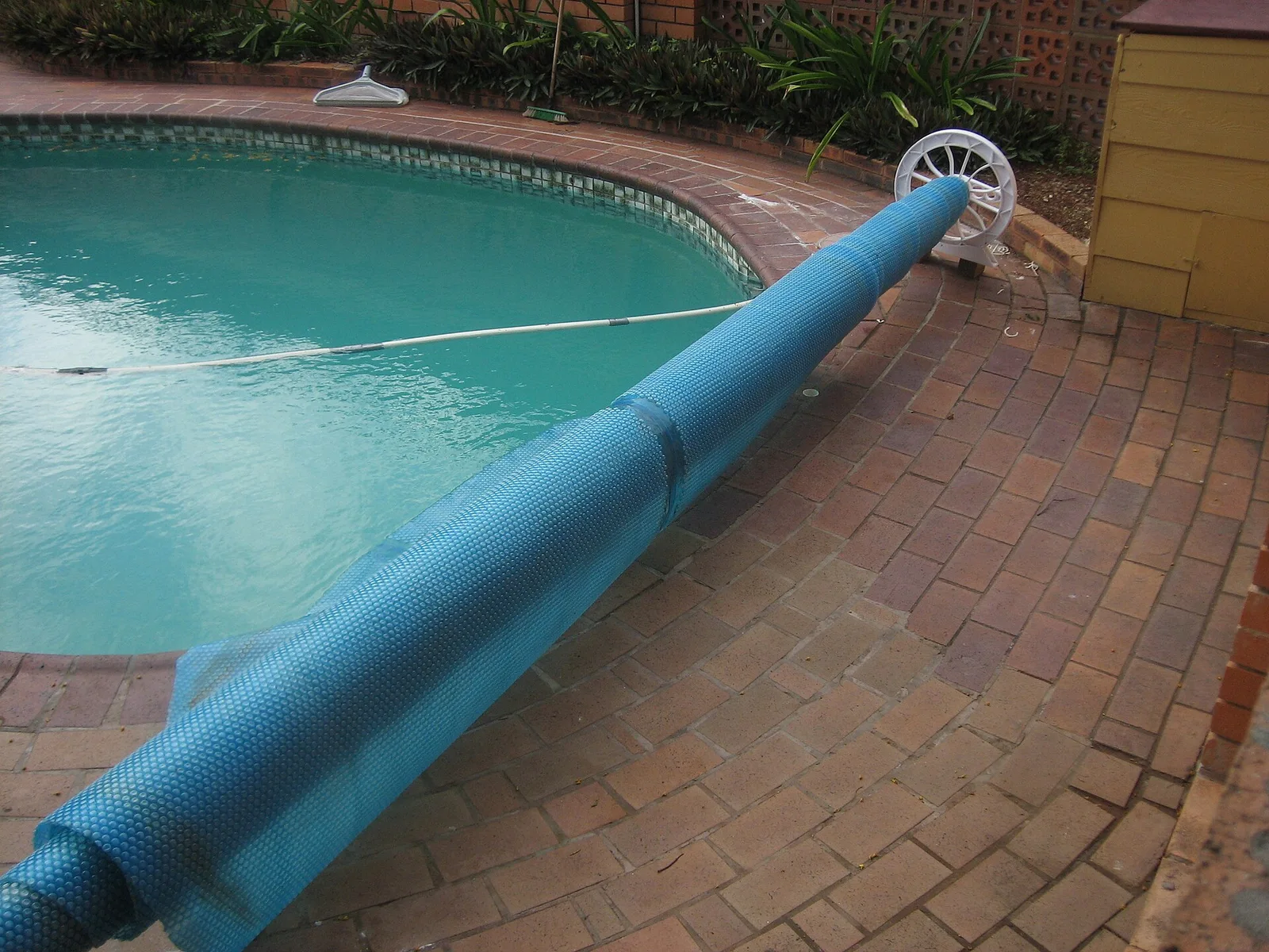 Blue solar pool cover rolled on a reel beside an empty residential swimming pool