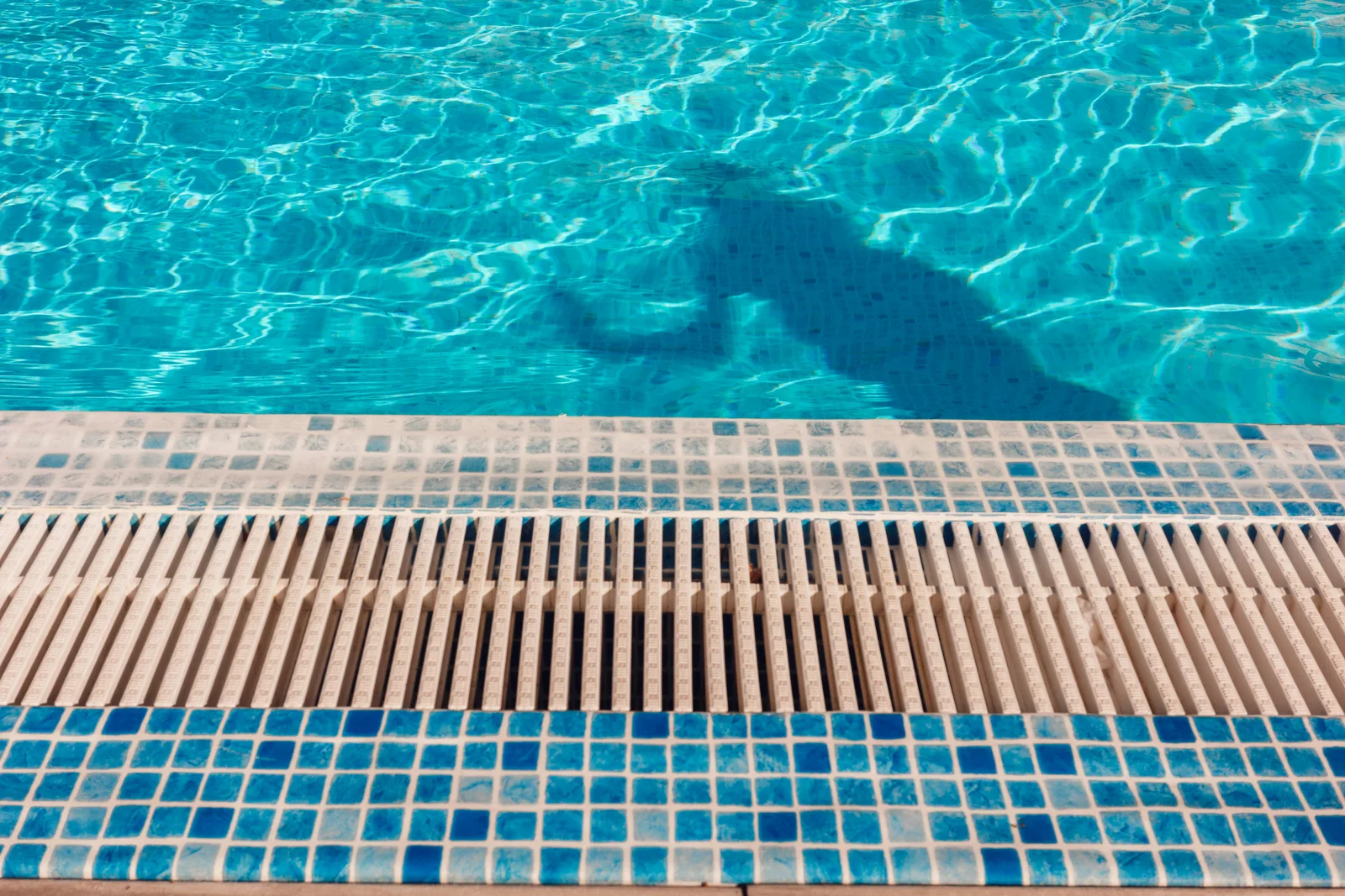 Clear pool water beside a tiled edge and narrow overflow drain