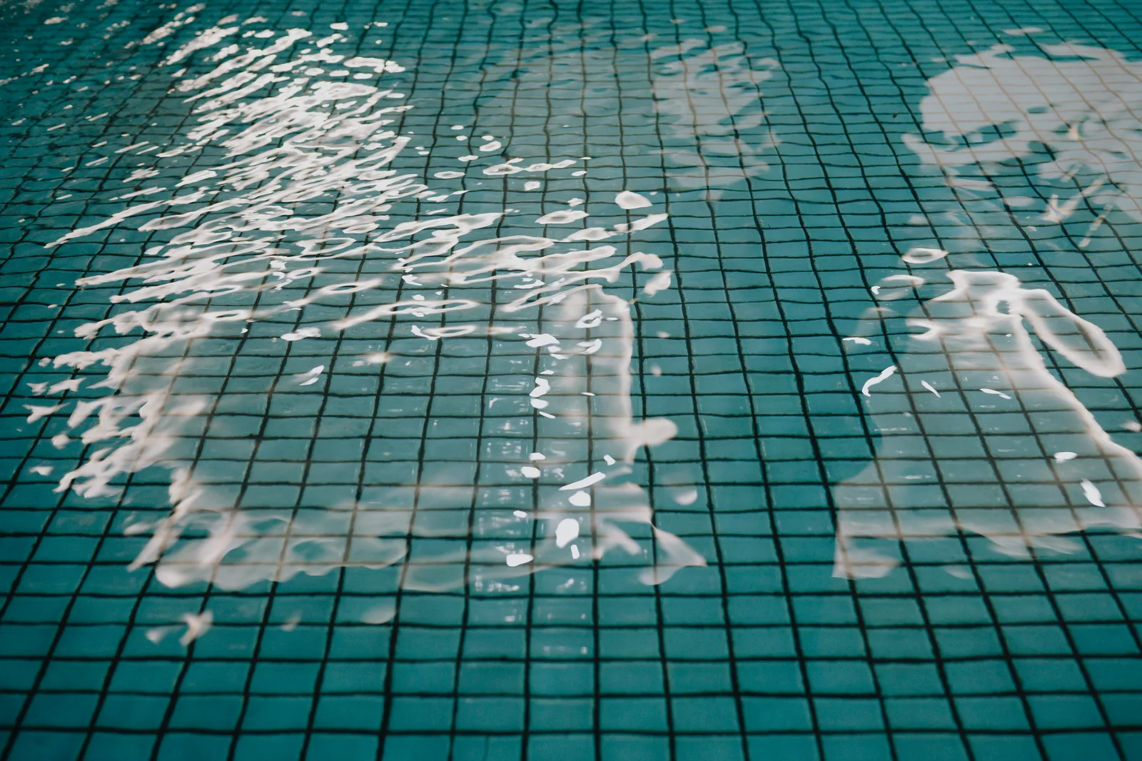 Sunlit ripples moving across small square tiles beneath clear pool water