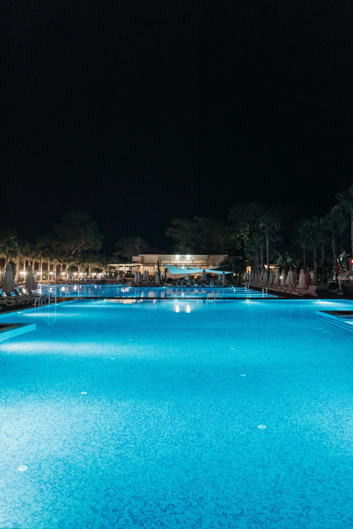 Empty outdoor swimming pool illuminated by multiple underwater lights at night