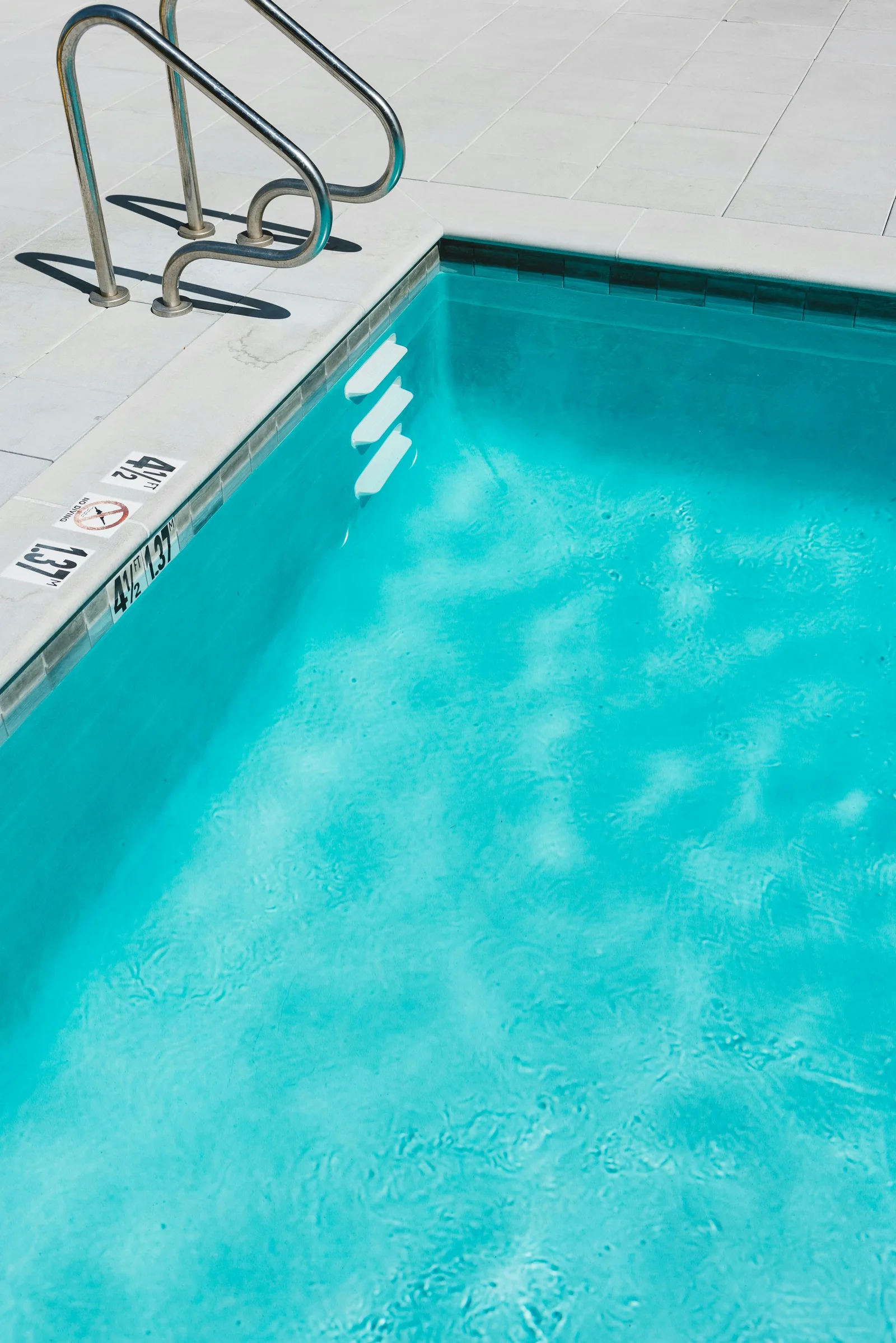 Clear blue swimming pool water rippling beside white steps and stainless steel rails