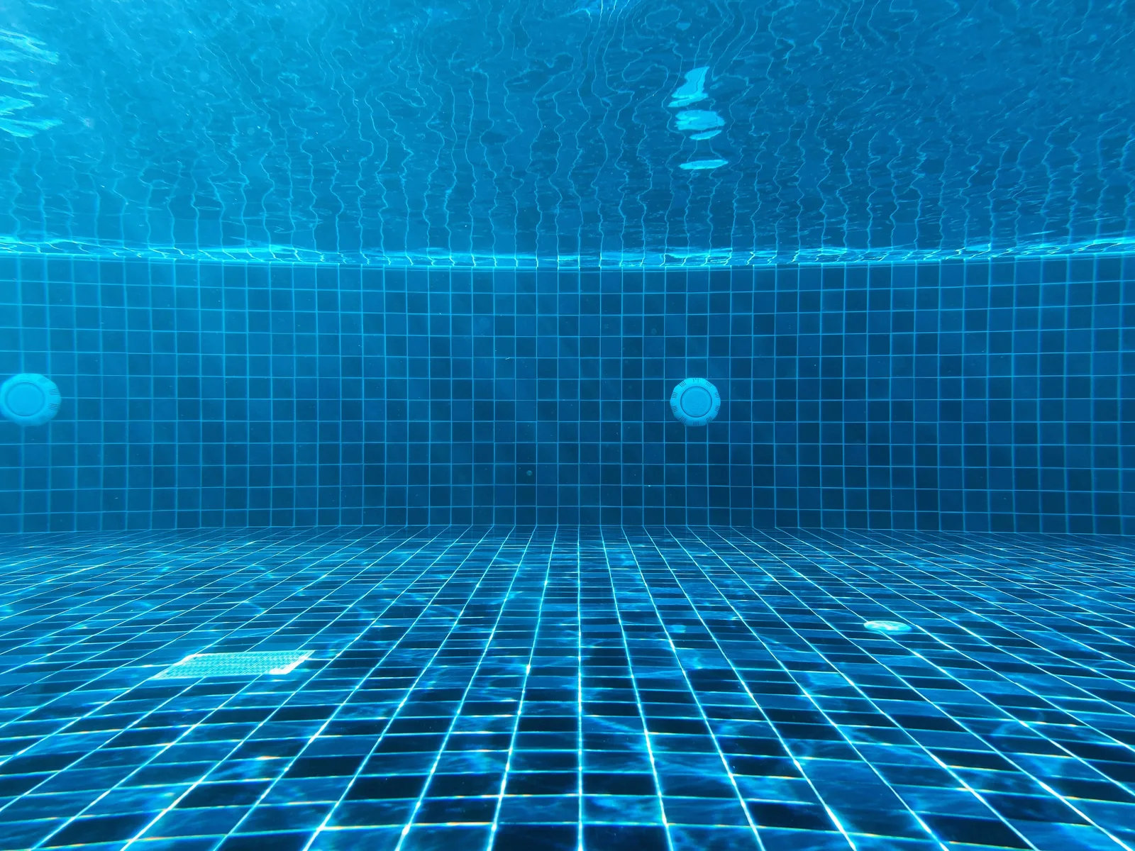 Two round return fittings on the tiled wall of an empty swimming pool