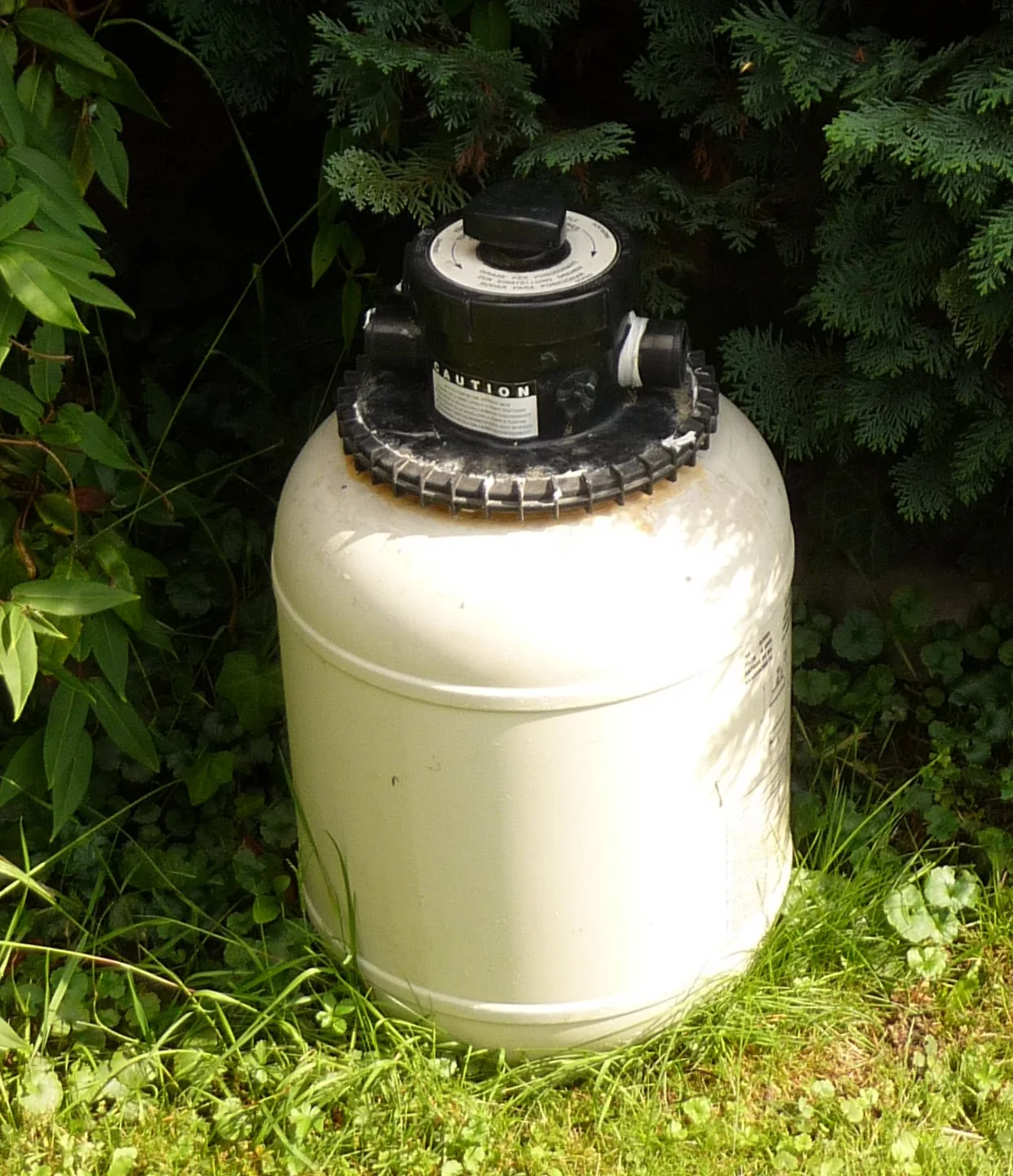 Outdoor sand filter with a multiport valve surrounded by green landscaping