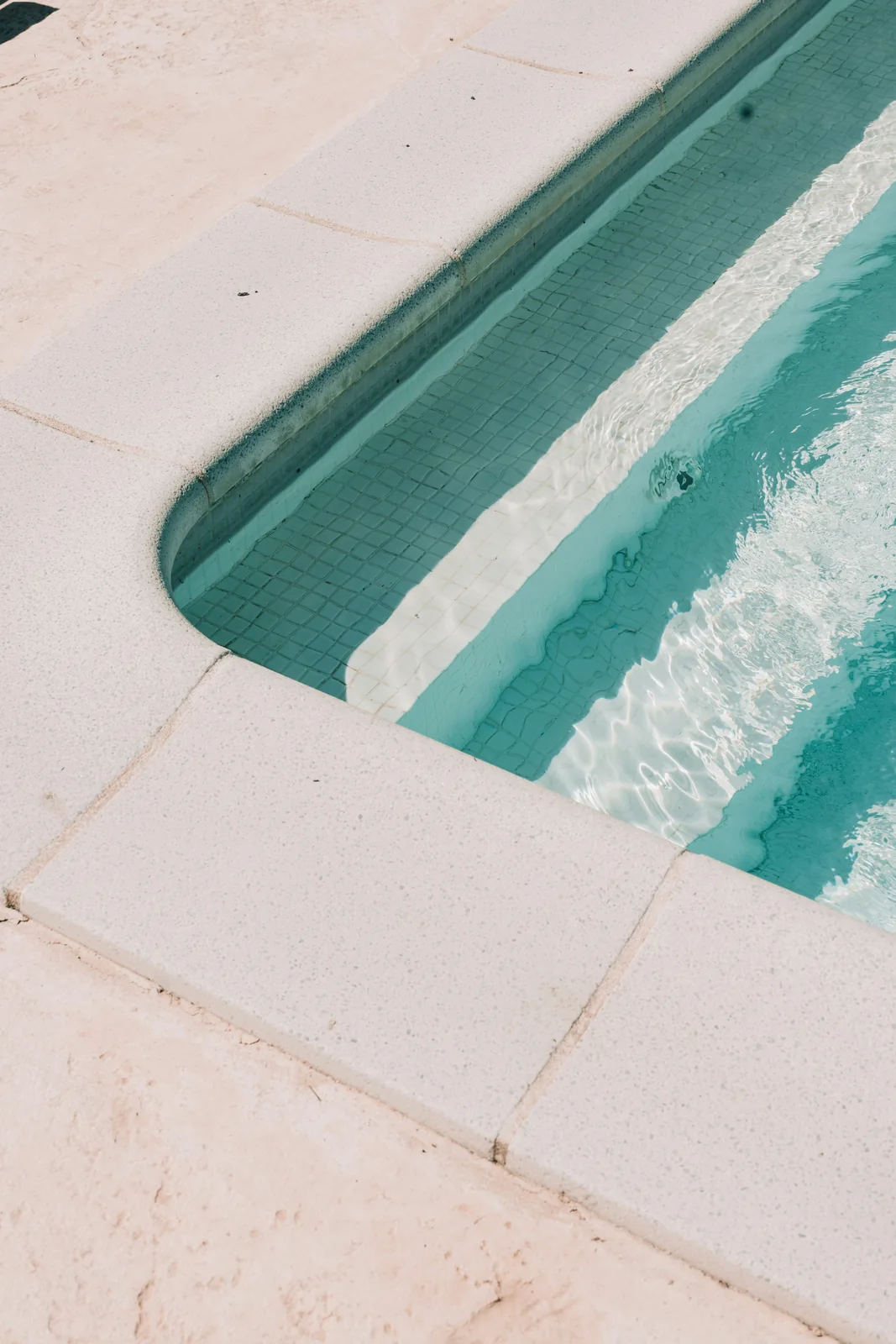 Clear turquoise pool water beside submerged tiled steps and pale coping